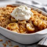Banana cobbler with golden crispy topping and whipped cream showing caramelized banana filling