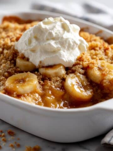 Banana cobbler with golden crispy topping and whipped cream showing caramelized banana filling