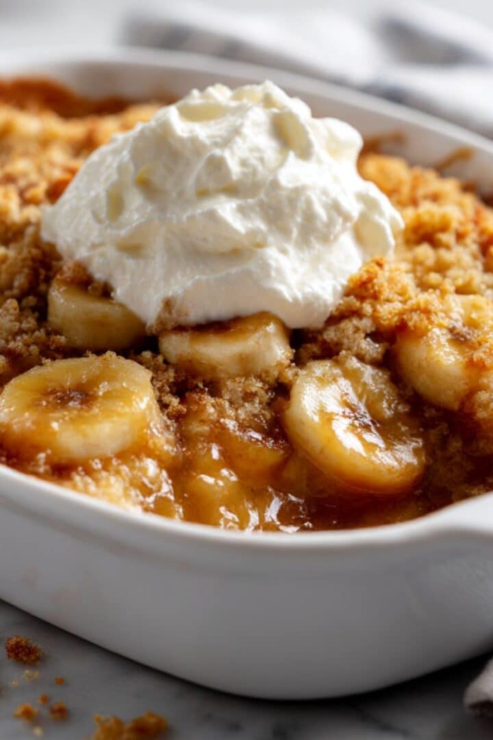 Banana cobbler with golden crispy topping and whipped cream showing caramelized banana filling