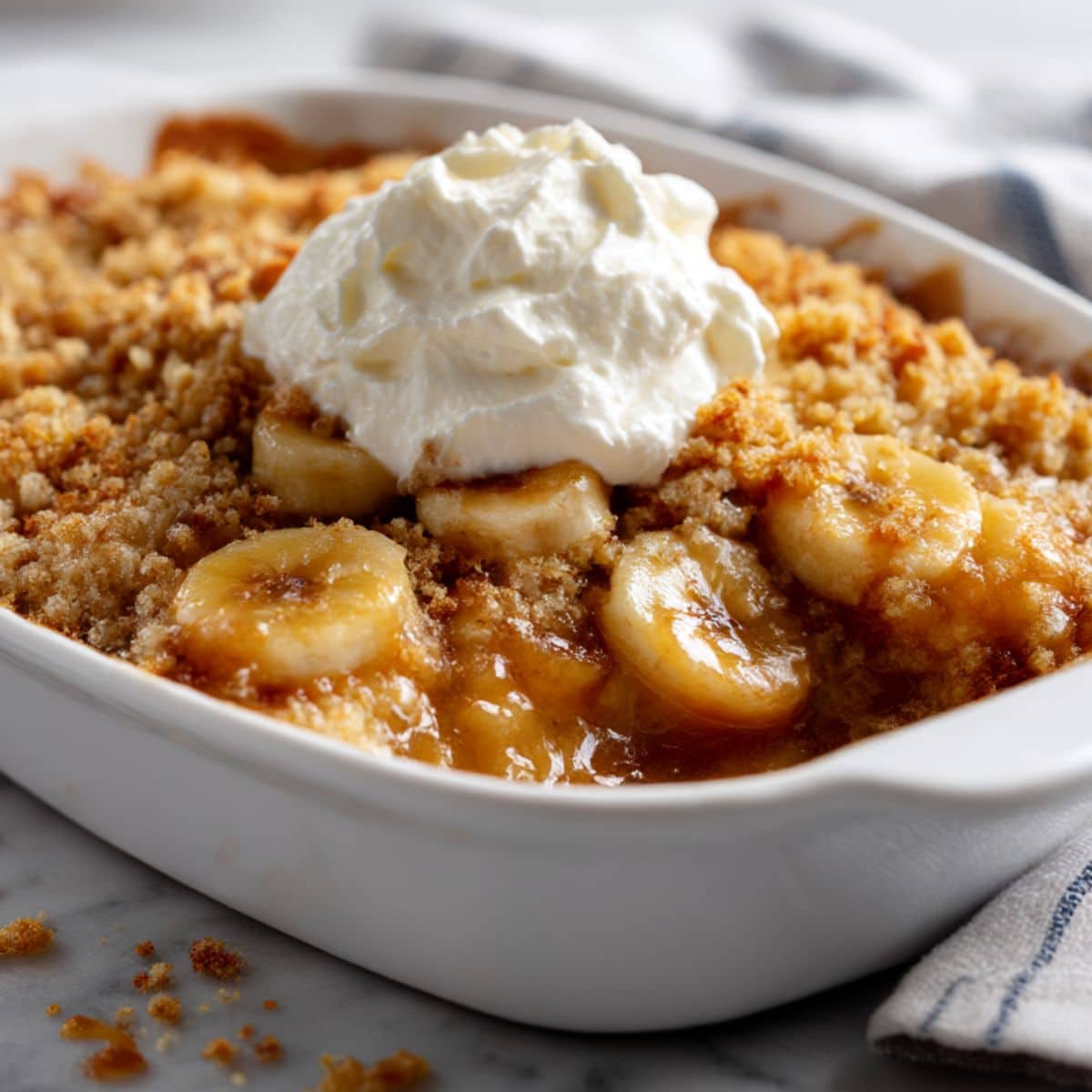 Banana cobbler with golden crispy topping and whipped cream showing caramelized banana filling