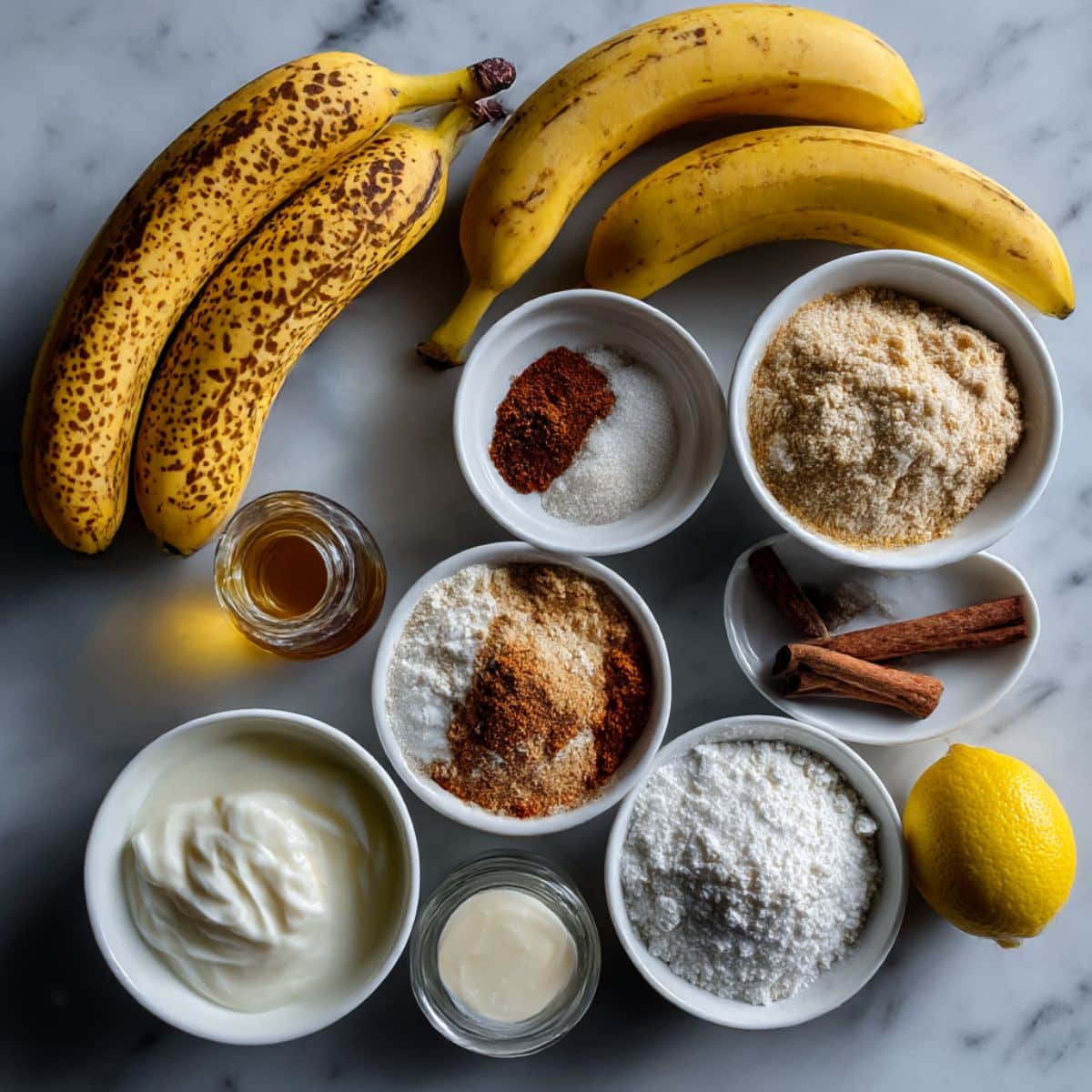 Overhead view of ingredients for banana cobbler on white counter. Includes ripe bananas, sugars, flour, butter, spices, and milk.