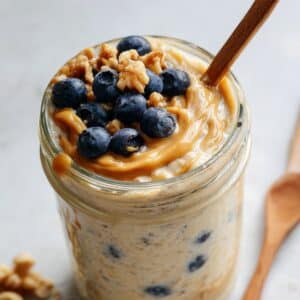 Homemade blended oats recipe in mason jar topped with fresh blueberries and chopped walnuts on white counter.