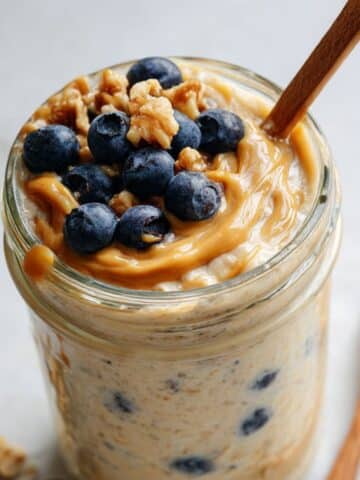 Homemade blended oats recipe in mason jar topped with fresh blueberries and chopped walnuts on white counter.