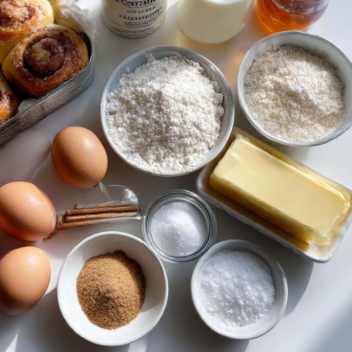 Overhead view of ingredients for cinnamon roll french toast bites including eggs, milk, cinnamon rolls, sugar, and maple syrup.