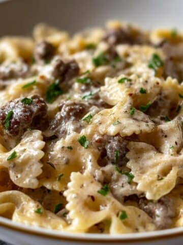 Creamy beef and bowtie pasta coated in rich Alfredo sauce, topped with fresh parsley and served in a white bowl on a marble countertop.