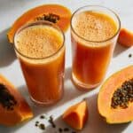 Two glasses of fresh homemade papaya juice with vibrant orange color and natural foam bubbles.