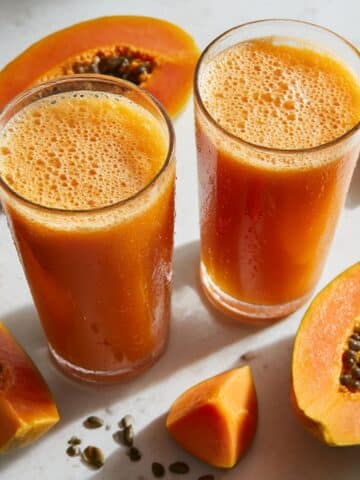 Two glasses of fresh homemade papaya juice with vibrant orange color and natural foam bubbles.