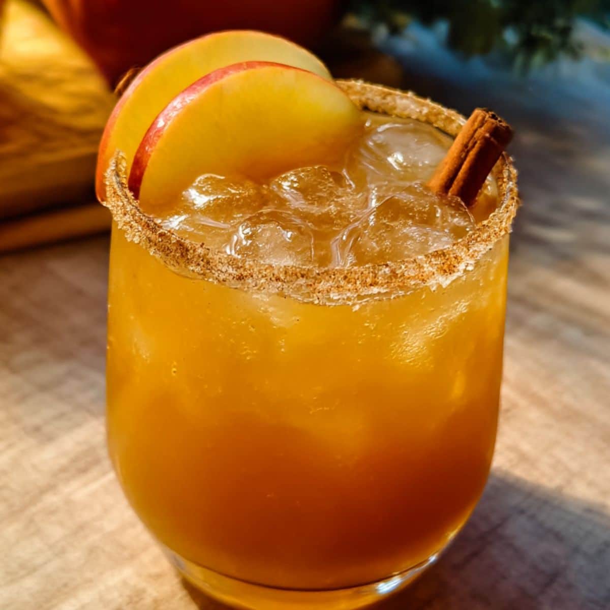 Apple cider margarita with cinnamon sugar rim, apple slices, and cinnamon stick served over ice in a glass.