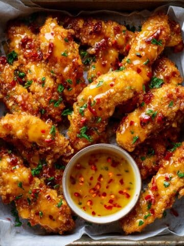 crispy Bang Bang Chicken tenders in a rustic tray, glazed with glossy spicy sauce, garnished with parsley, and served with a creamy chili dipping sauce in a ramekin.