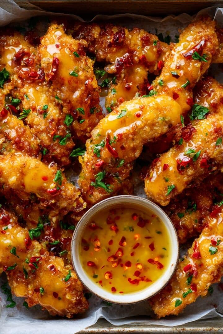 crispy Bang Bang Chicken tenders in a rustic tray, glazed with glossy spicy sauce, garnished with parsley, and served with a creamy chili dipping sauce in a ramekin.