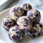 Homemade blueberry protein balls with oats, almond butter, and vibrant purple blueberry swirls on a white plate.