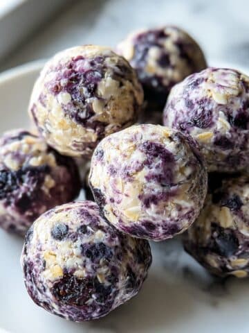 Homemade blueberry protein balls with oats, almond butter, and vibrant purple blueberry swirls on a white plate.