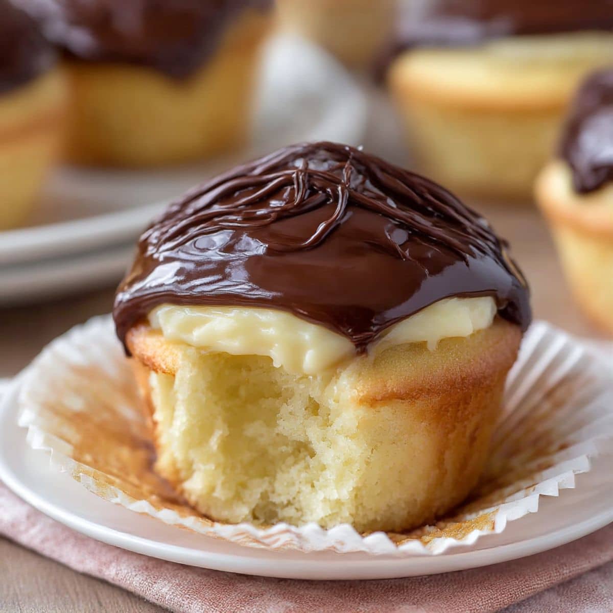 Boston cream pie cupcake filled with vanilla custard and topped with glossy chocolate ganache.