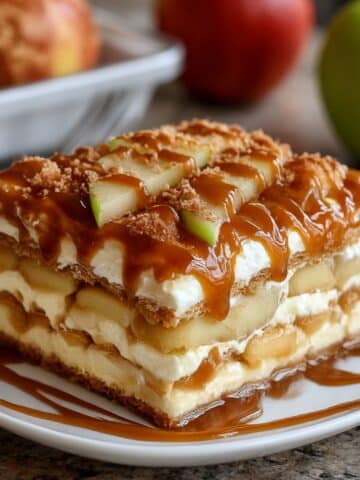 Slice of homemade caramel apple eclair cake layered with apples, pudding, and graham crackers. Topped with caramel drizzle and fresh apple slices for a no bake dessert.