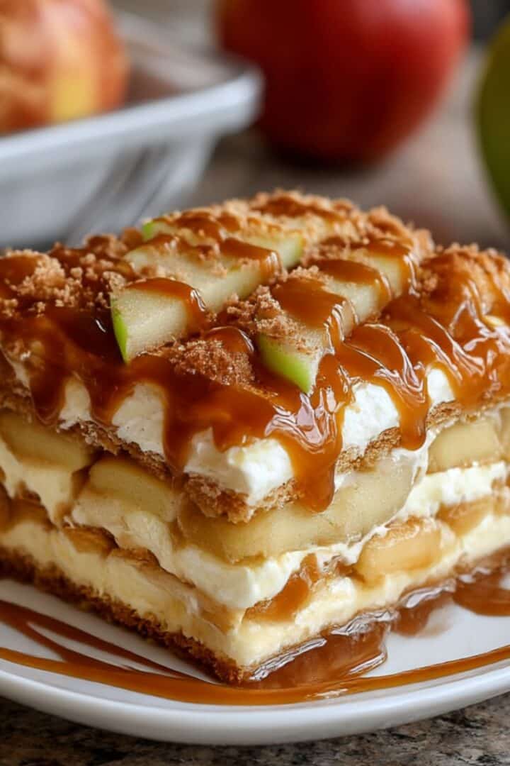 Slice of homemade caramel apple eclair cake layered with apples, pudding, and graham crackers. Topped with caramel drizzle and fresh apple slices for a no bake dessert.