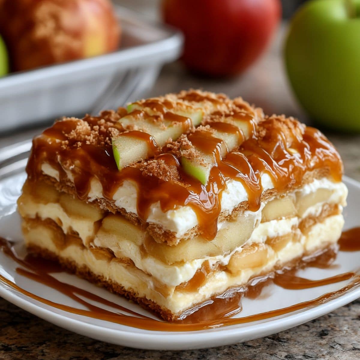 Slice of homemade caramel apple eclair cake layered with apples, pudding, and graham crackers. Topped with caramel drizzle and fresh apple slices for a no bake dessert.