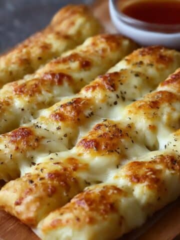 Golden homemade cheesy breadsticks topped with garlic butter and herbs, served with marinara sauce