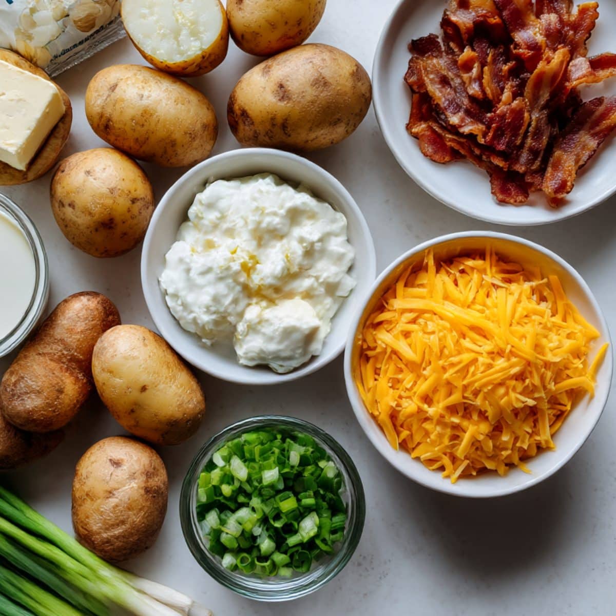 Ingredients for cheesy Mississippi Mud potatoes including baby potatoes, cheddar, cream cheese, sour cream, bacon, and ranch mix on a white counter.
