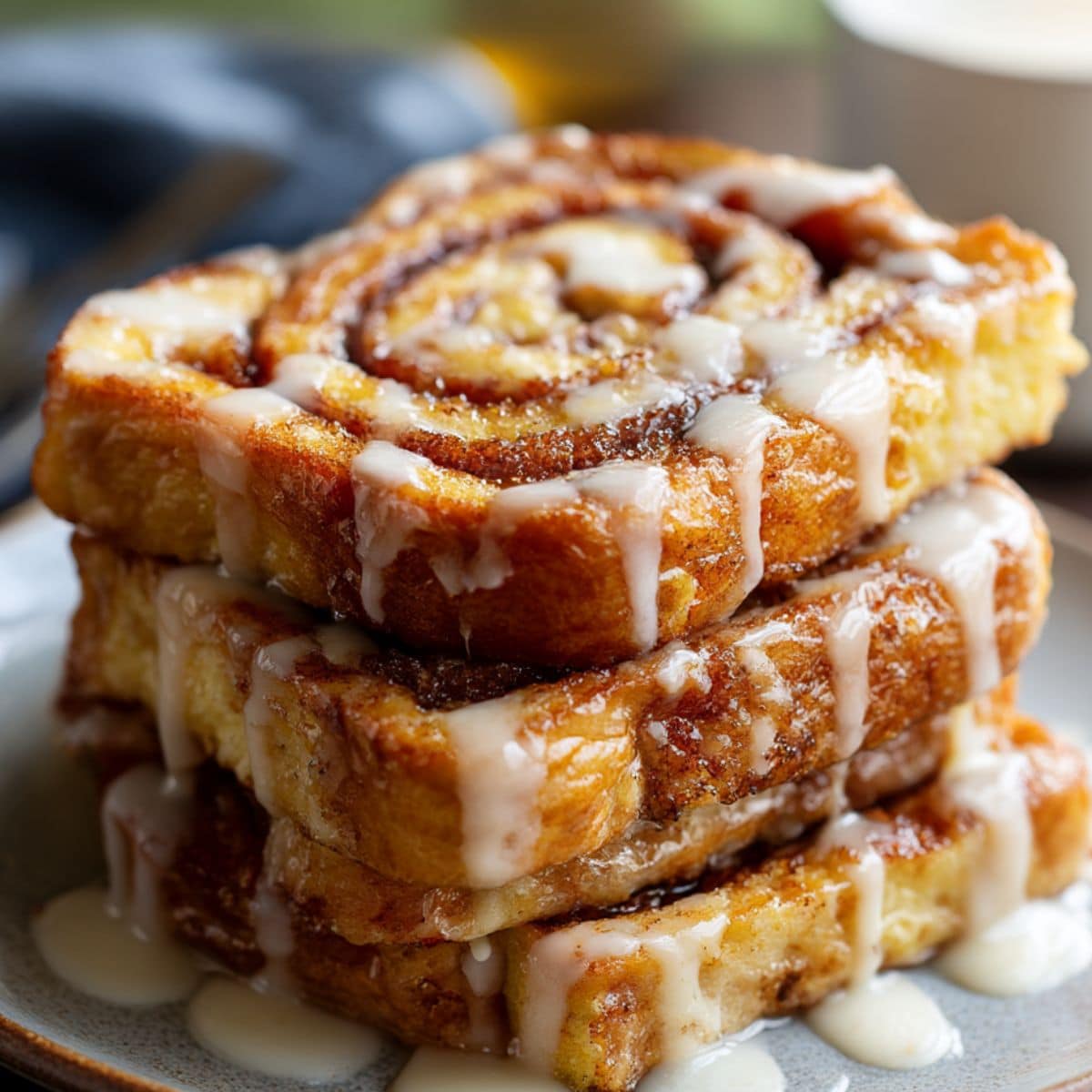 Caramelized cinnamon roll French toast slices stacked on a plate, swirled with cinnamon sugar and topped with icing glaze, golden-brown edges with a sticky, juicy finish.