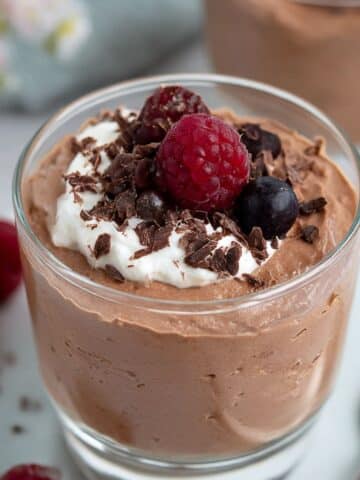 Homemade cottage cheese chocolate mousse in a glass topped with whipped cream, raspberries, and dark chocolate shavings.