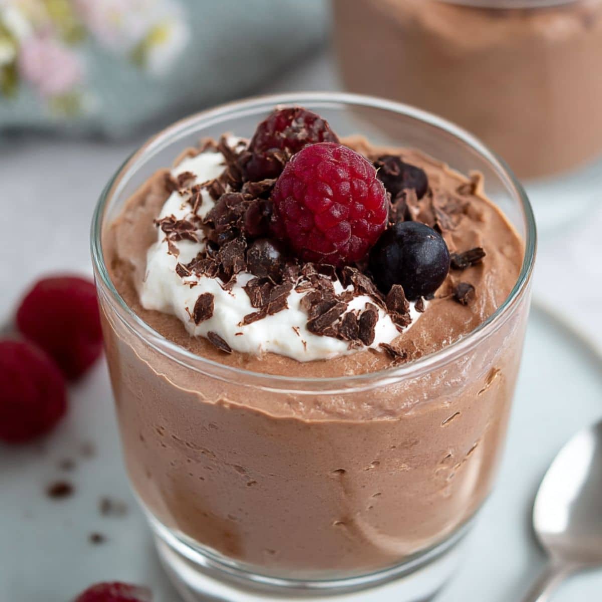 Homemade cottage cheese chocolate mousse in a glass topped with whipped cream, raspberries, and dark chocolate shavings.