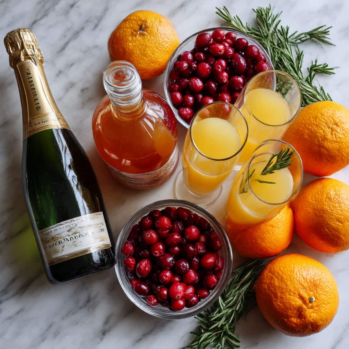 Overhead view of cranberry mimosa ingredients including Prosecco, cranberry juice, oranges, and rosemary.