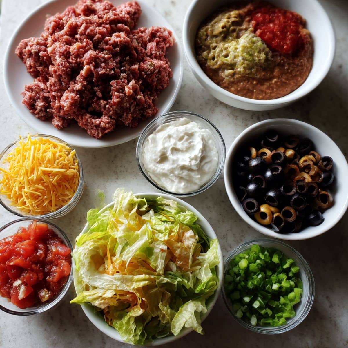 Overhead photo of crescent roll taco pizza ingredients, including beef, beans, cheese, lettuce, tomatoes, and toppings.