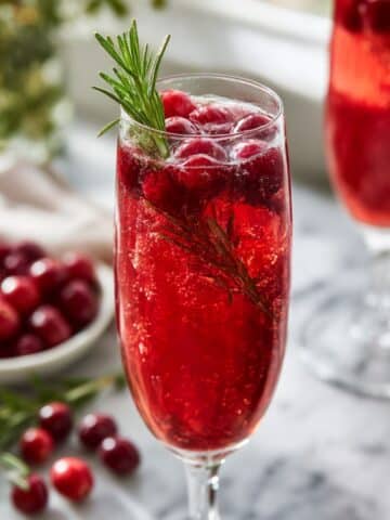 Sparkling cranberry mimosa made with Prosecco, cranberry juice, and fresh rosemary sprigs.