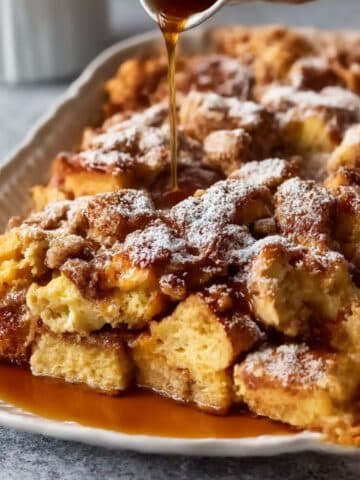 Golden baked french toast casserole topped with powdered sugar and warm syrup drizzle.