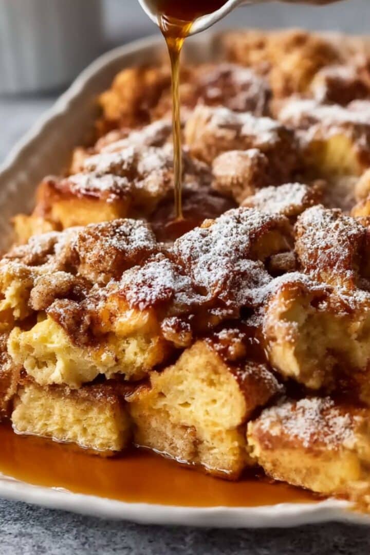 Golden baked french toast casserole topped with powdered sugar and warm syrup drizzle.