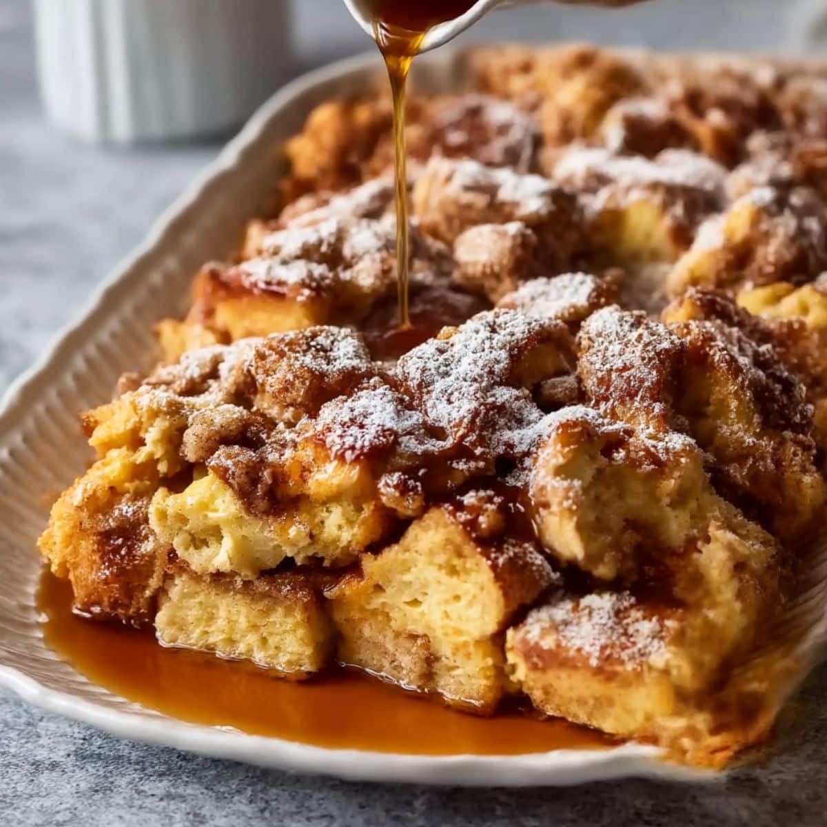 Golden baked french toast casserole topped with powdered sugar and warm syrup drizzle.