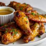 Sticky honey mustard chicken wings coated in a thick, glossy glaze, garnished with fresh chopped parsley and served on a white plate with a ramekin of dipping sauce in the background.