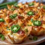 Golden crispy jalapeño popper wonton cups filled with creamy cheese, bacon, and jalapeños, topped with melted cheddar and sliced green onions.