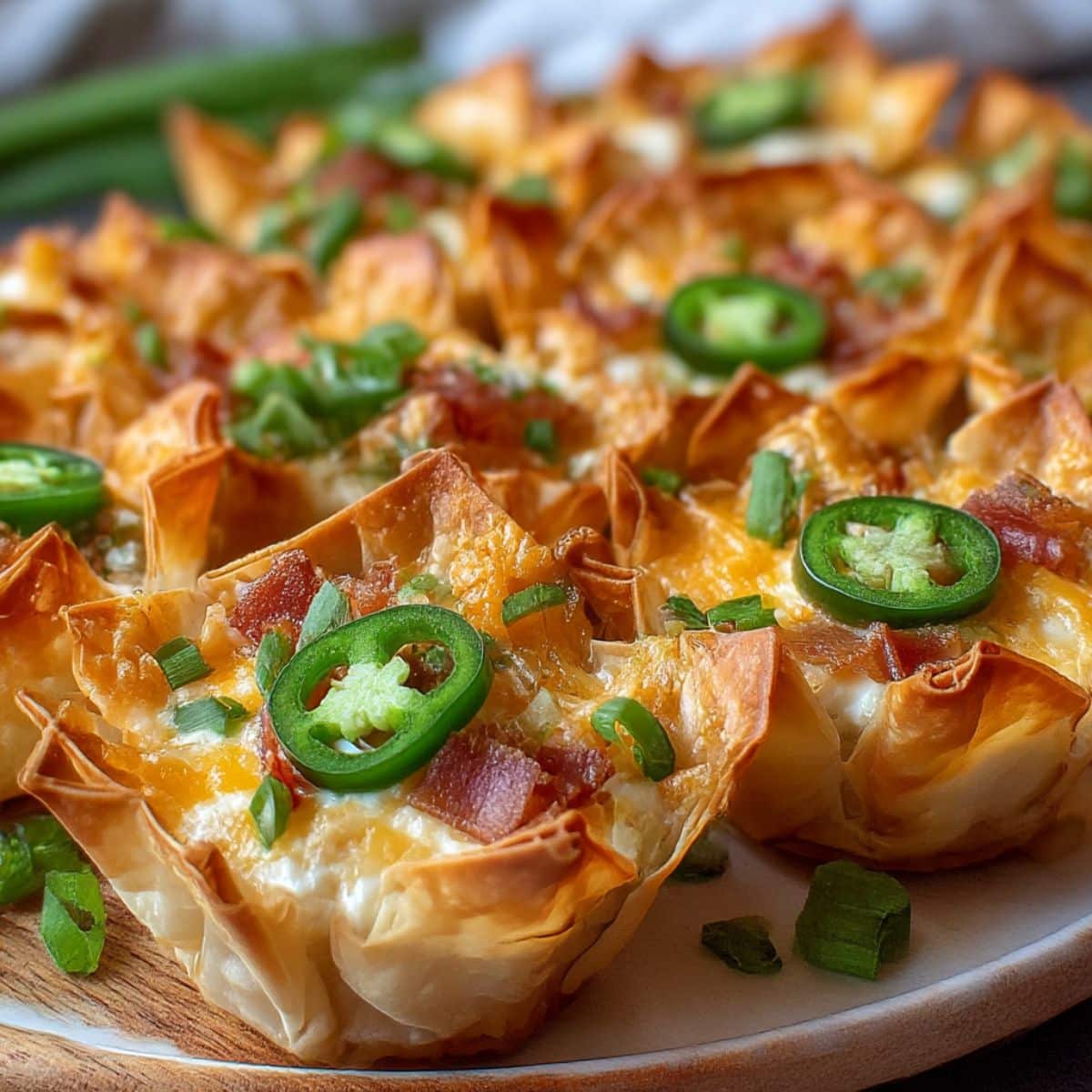 Golden crispy jalapeño popper wonton cups filled with creamy cheese, bacon, and jalapeños, topped with melted cheddar and sliced green onions.