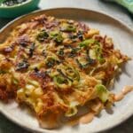 Crispy Japanese cabbage pancake topped with scallions and nori strips on a white plate.