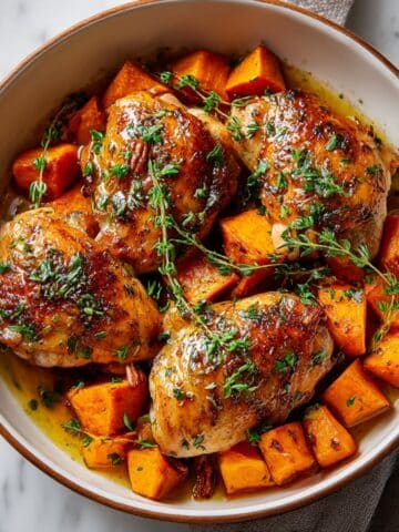 Maple glazed chicken with roasted sweet potatoes topped with chopped pecans and fresh thyme, coated in glossy maple Dijon glaze for a cozy fall dinner.