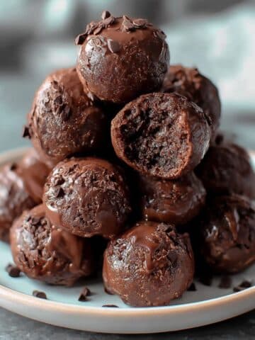 Homemade no bake brownie bites stacked on a white plate with a glossy chocolate coating.