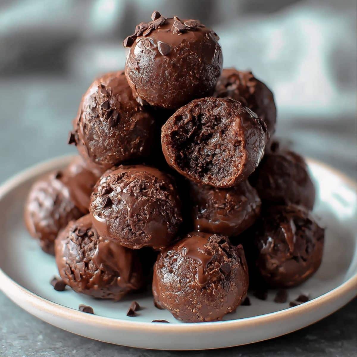 Homemade no bake brownie bites stacked on a white plate with a glossy chocolate coating.