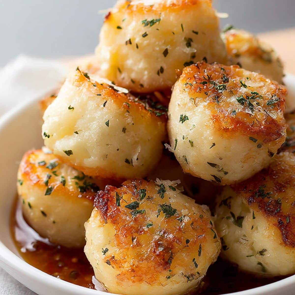 Golden parmesan bread bites brushed with garlic butter and sprinkled with herbs, served warm in a white bowl.