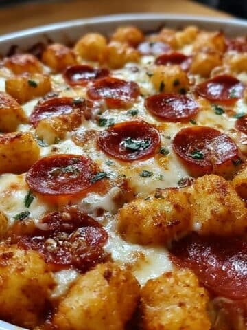 Cheesy pizza tater tot casserole topped with crispy golden tater tots, melted mozzarella, mini pepperoni slices, and fresh herbs, baked to bubbly perfection in a white casserole dish.