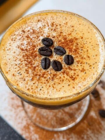 Pumpkin spice espresso martini topped with creamy foam, cinnamon dusting, and coffee beans.