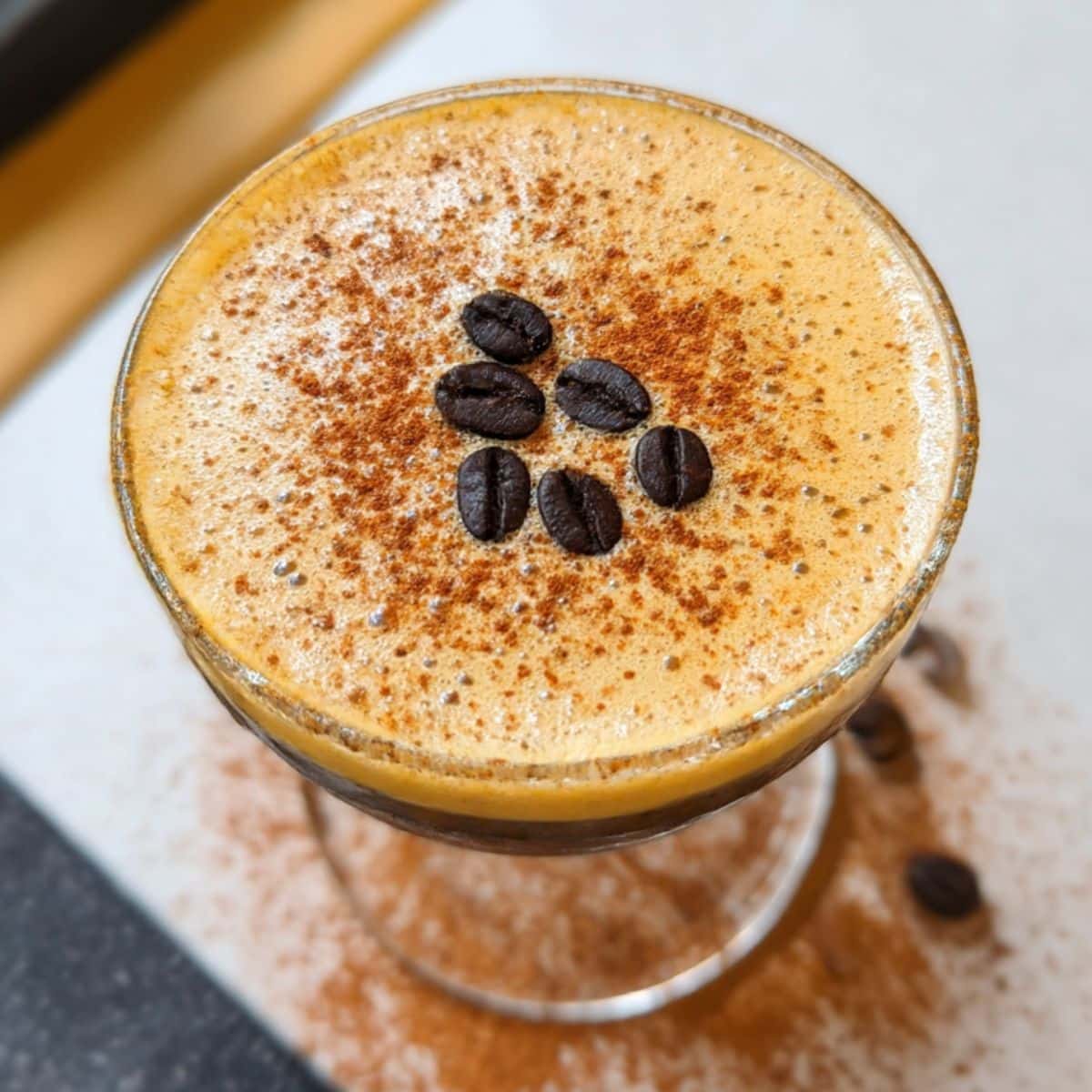 Pumpkin spice espresso martini topped with creamy foam, cinnamon dusting, and coffee beans.