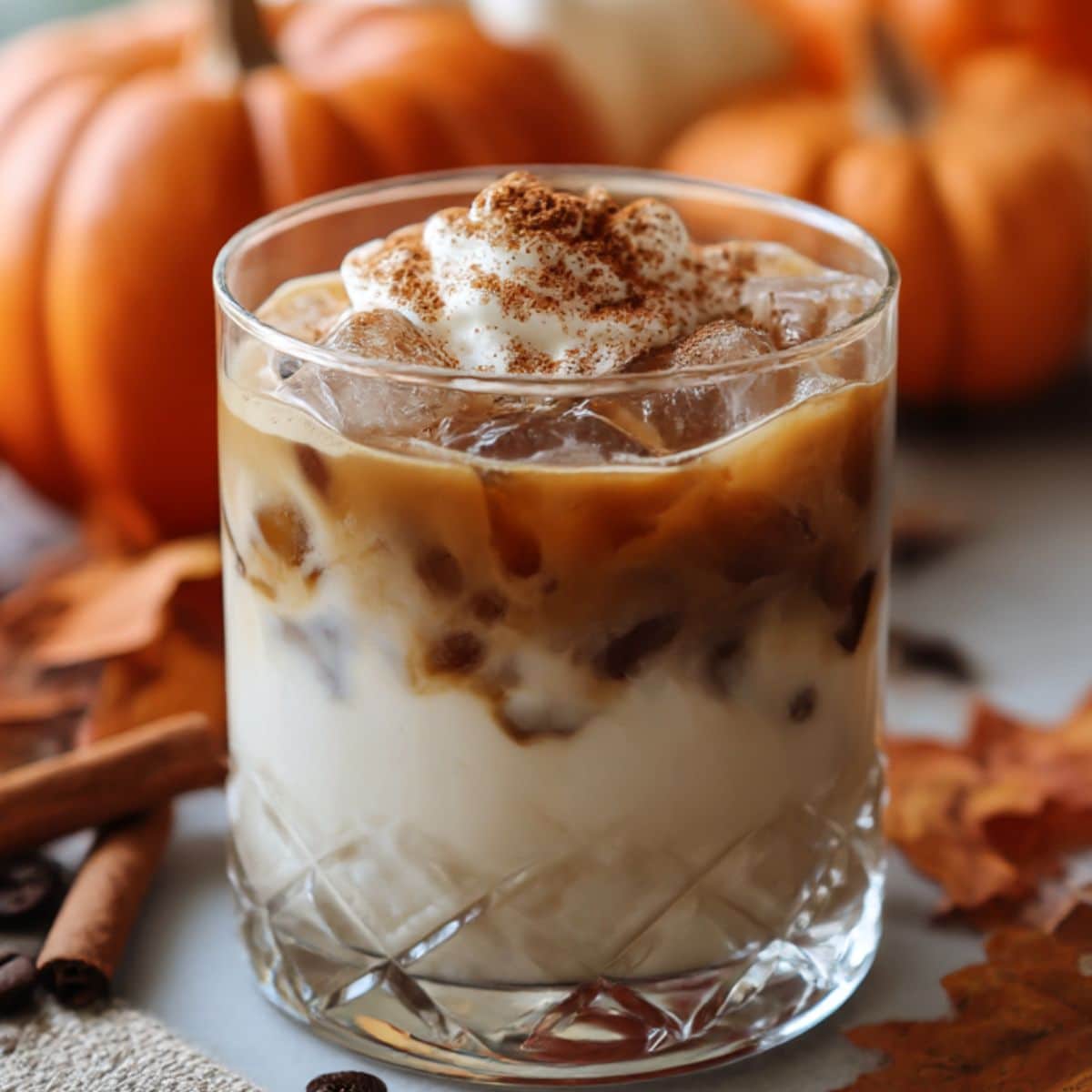 Pumpkin spice white russian cocktail over ice topped with whipped cream and cinnamon, surrounded by pumpkins and fall leaves.