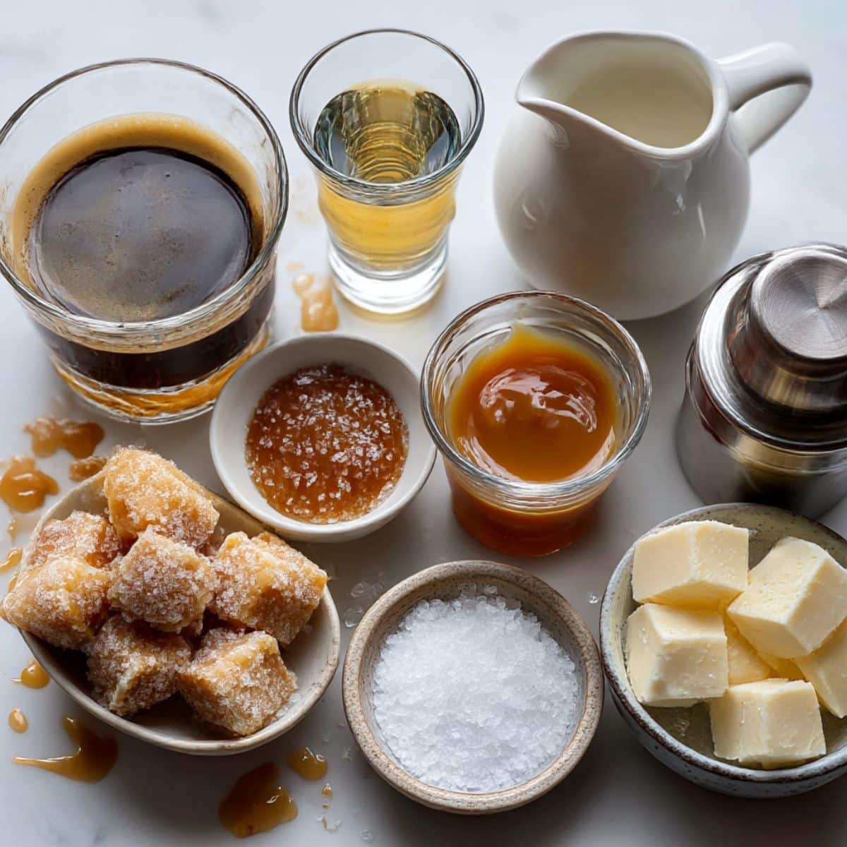 All ingredients for homemade salted caramel espresso martini on a white counter, including espresso, vodka, coffee liqueur, caramel sauce, sea salt, cream, and ice.