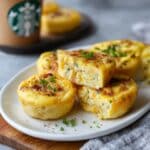 Fluffy copycat Starbucks egg bites with bacon and Gruyere cheese stacked on white plate, easy homemade high protein breakfast recipe