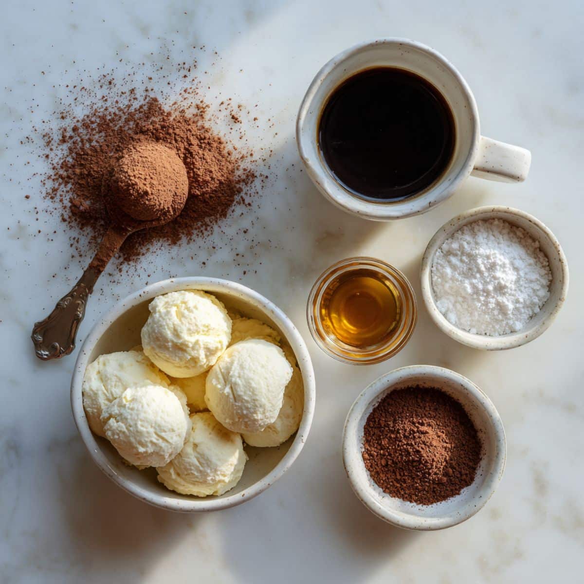 Ingredients for tiramisu truffles on a white kitchen counter with mascarpone, ladyfingers, and cocoa powder