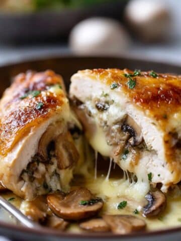 Cheesy garlic butter mushroom stuffed chicken breast cut open to show melty cheese and sautéed mushrooms on a plate.
