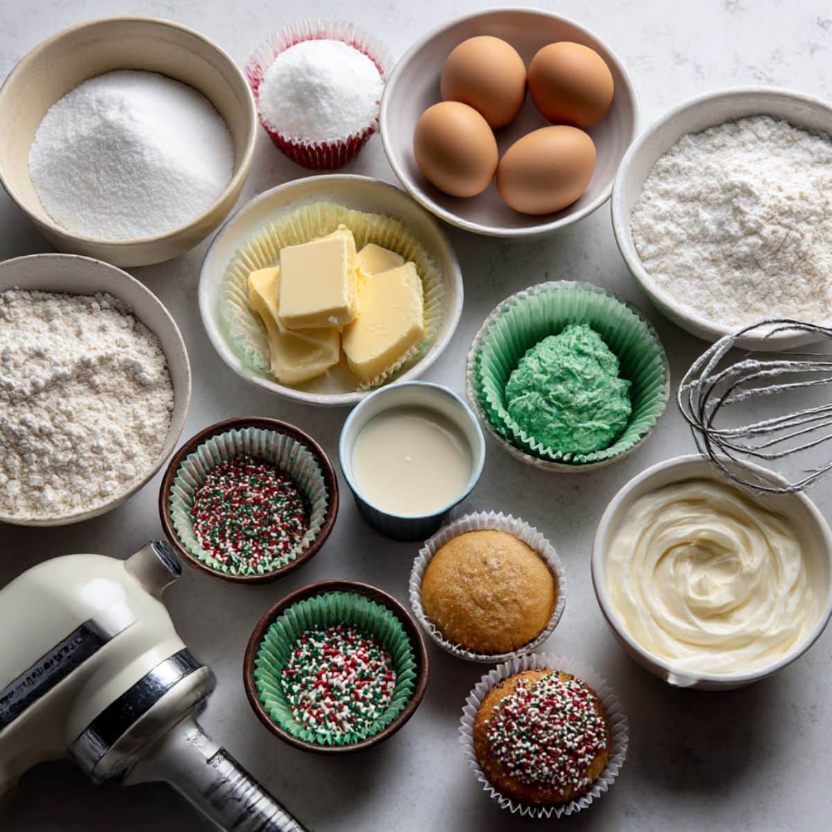 Overhead view of Christmas tree cupcake ingredients arranged casually on a white kitchen counter.