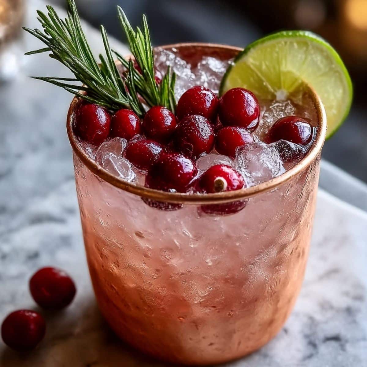 Holiday mule cocktail in a copper mug with cranberries, rosemary, lime, and crushed ice.