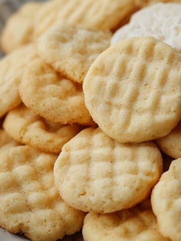 Soft mini sugar cookies with golden edges and fork-pressed tops stacked on a plate.